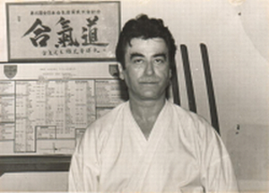 John A. Havan in a dojo, standing before an Aikido calligraphy scroll